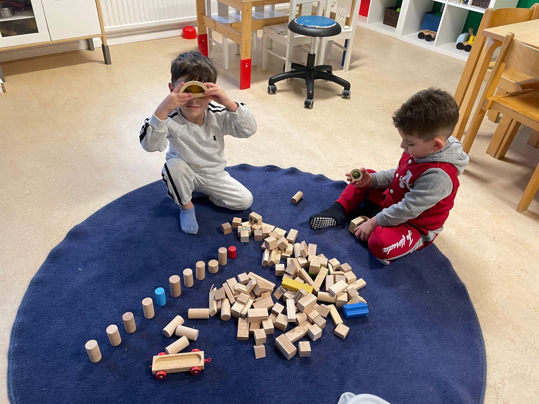 Barn som ritar tillsammans vid ett lågt träbord medan en pedagog finns närvarande i bakgrunden